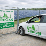 SecuConCept Sicherheitsdienstfahrzeug mit einem Mitarbeiter an einem gesicherten Objekt mit Solarpanelen im Hintergrund.