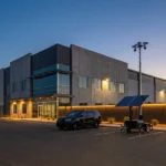 Moderne Lagerhalle mit einer Überwachungskamera und einem Solarpanel auf einem Parkplatz bei Dämmerung.