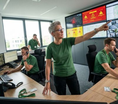 In der modernen Leitstelle für Alarmverfolgung 2026 koordinieren mehrere Mitarbeitende Telefongespräche, Kamerabilder und Alarme an großen Monitorwänden.