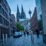 Vor dem Kölner Dom patrouillieren Sicherheitskräfte in einer engen Straße zwischen modernen Gebäuden und roten Wandhydranten.