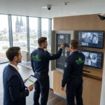 Drei Sicherheitsmitarbeiter prüfen am Empfang digitale Monitore und Zugangstechnik für einen serviceorientierten Sicherheitsdienst.