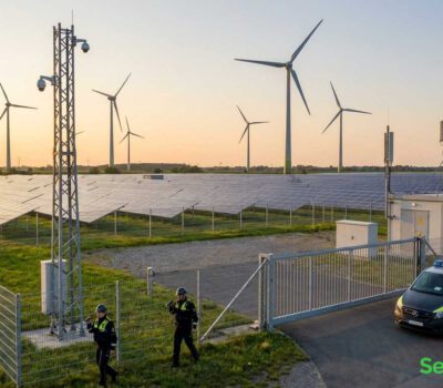 Windpark und Photovoltaik-Feld mit umzäuntem Zugang, Sicherheitsfahrzeug und zwei Sicherheitsmitarbeitern in NRW